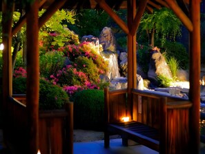 A wooden gazebo with a bench, surrounded by lush greenery and a small waterfall. - Chateraise Hotel Isawa (Fuefuki)