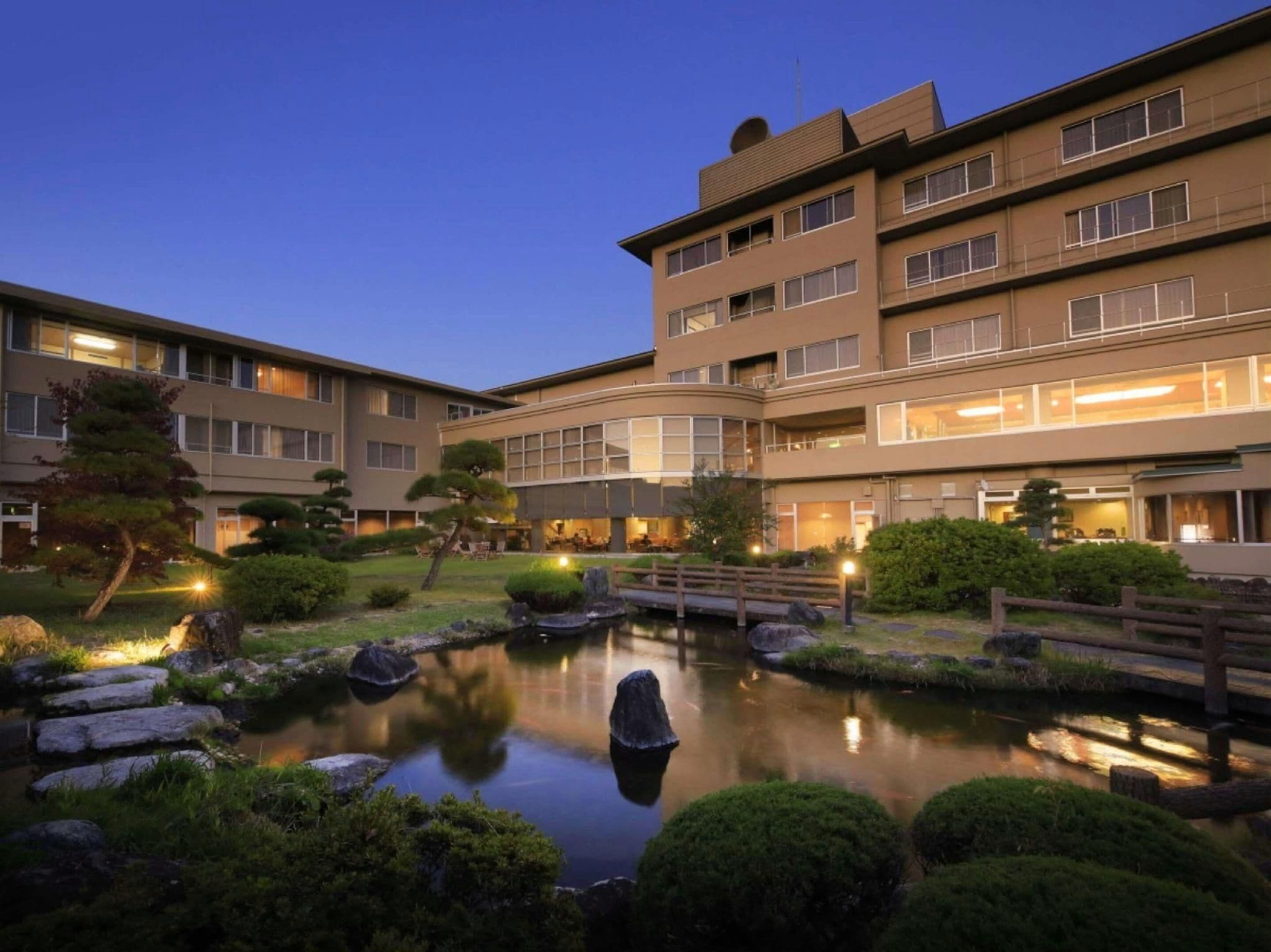 A multi-story hotel with a landscaped garden, including a pond and a wooden bridge.