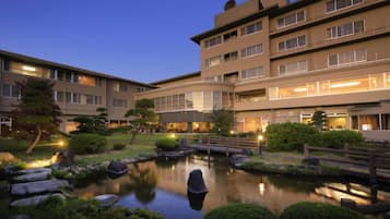 A multi-story hotel with a landscaped garden, including a pond and a wooden bridge.