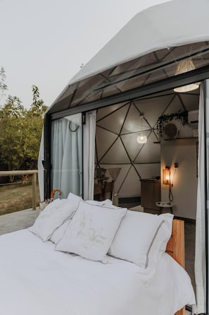 Quarto estilo tenda com cama, luminária pendente e um pequeno banheiro.