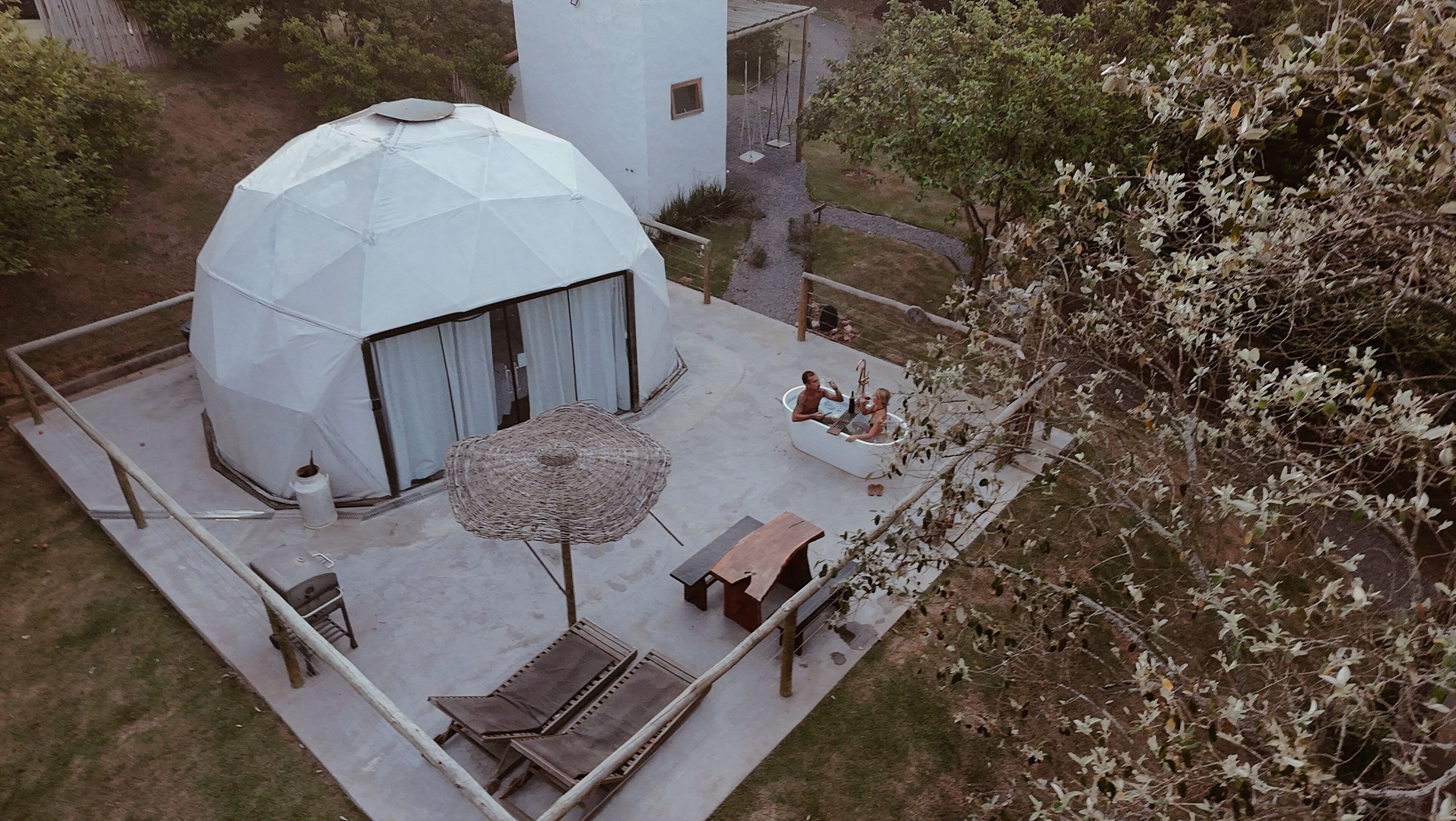 A geodesic dome structure with a covered patio area, outdoor seating, and a small tree.