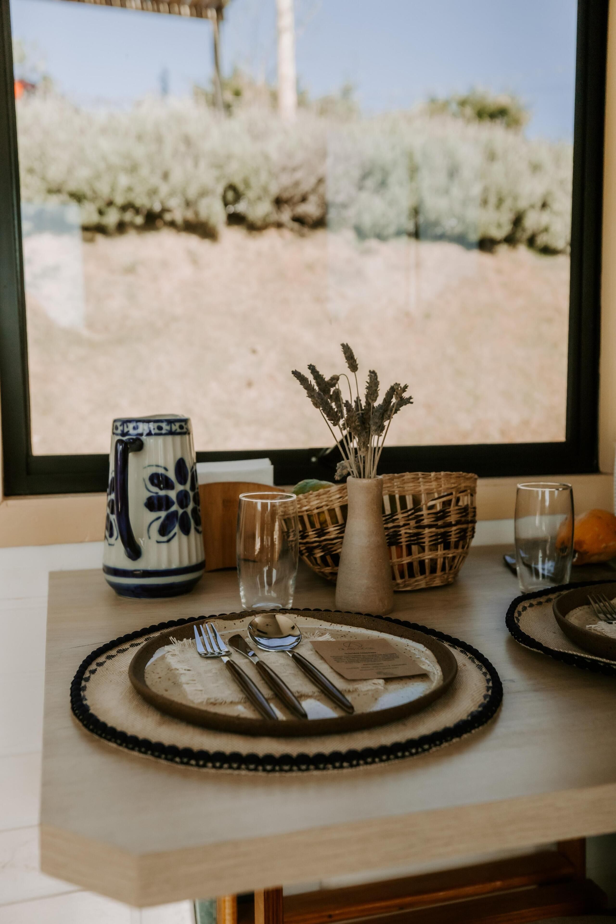 A dining table set with plates, cutlery, glasses, a vase with dried flowers, and a decorative pitcher.