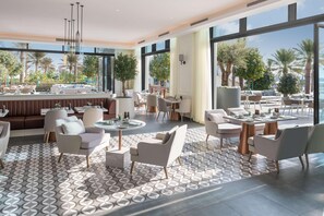 A modern indoor space with seating areas, large windows, and a view of palm trees. - Vida Beach Resort Marassi Al Bahrain (Manama)