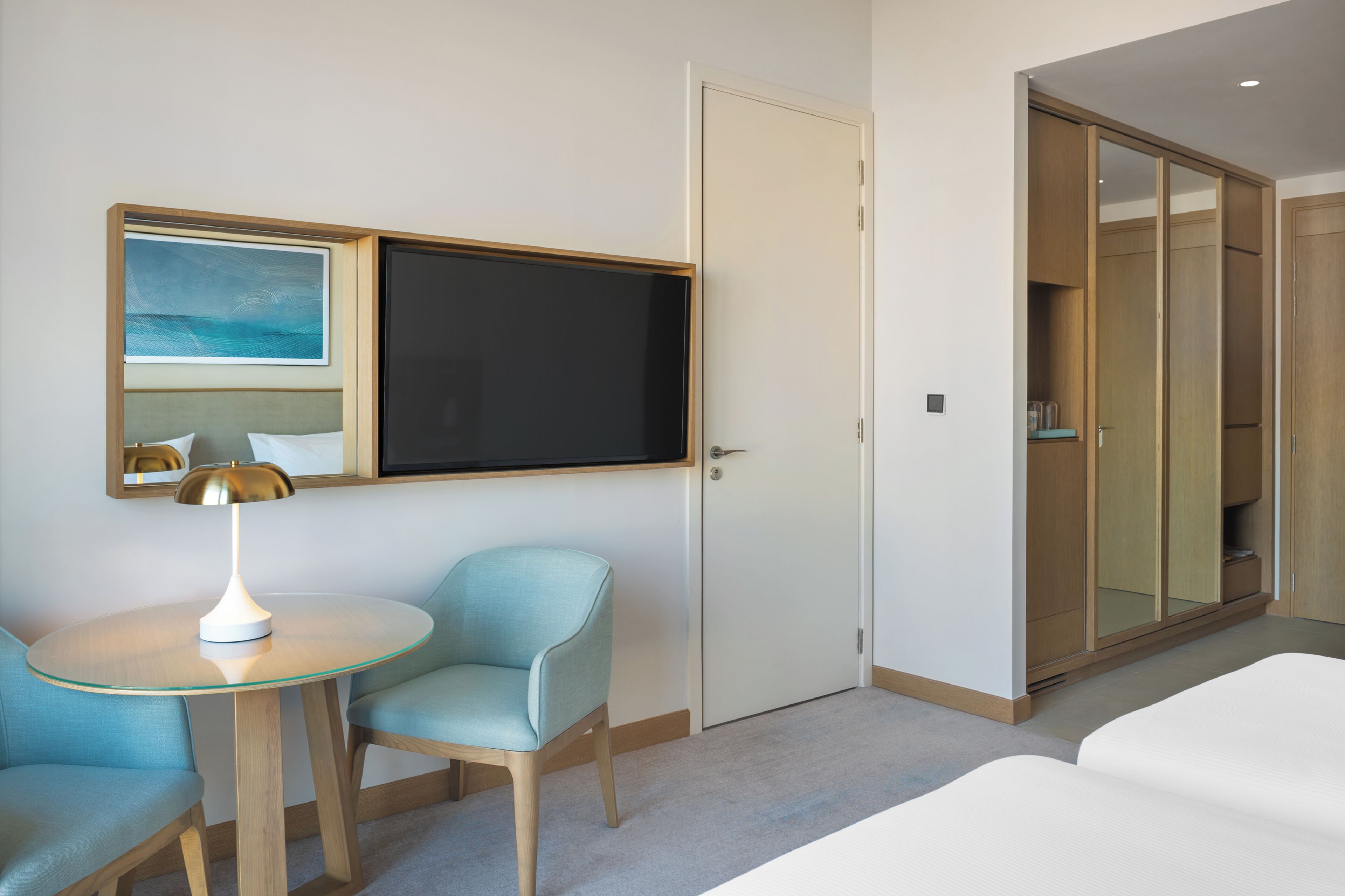 Ein Hotelzimmer mit einem Bett, einem Schreibtisch mit Lampe, einem Sessel, einem Fernseher und einem Kleiderschrank.