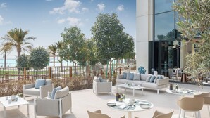 En udendørs patio med siddepladser, udsigt til havet og en moderne bygning.