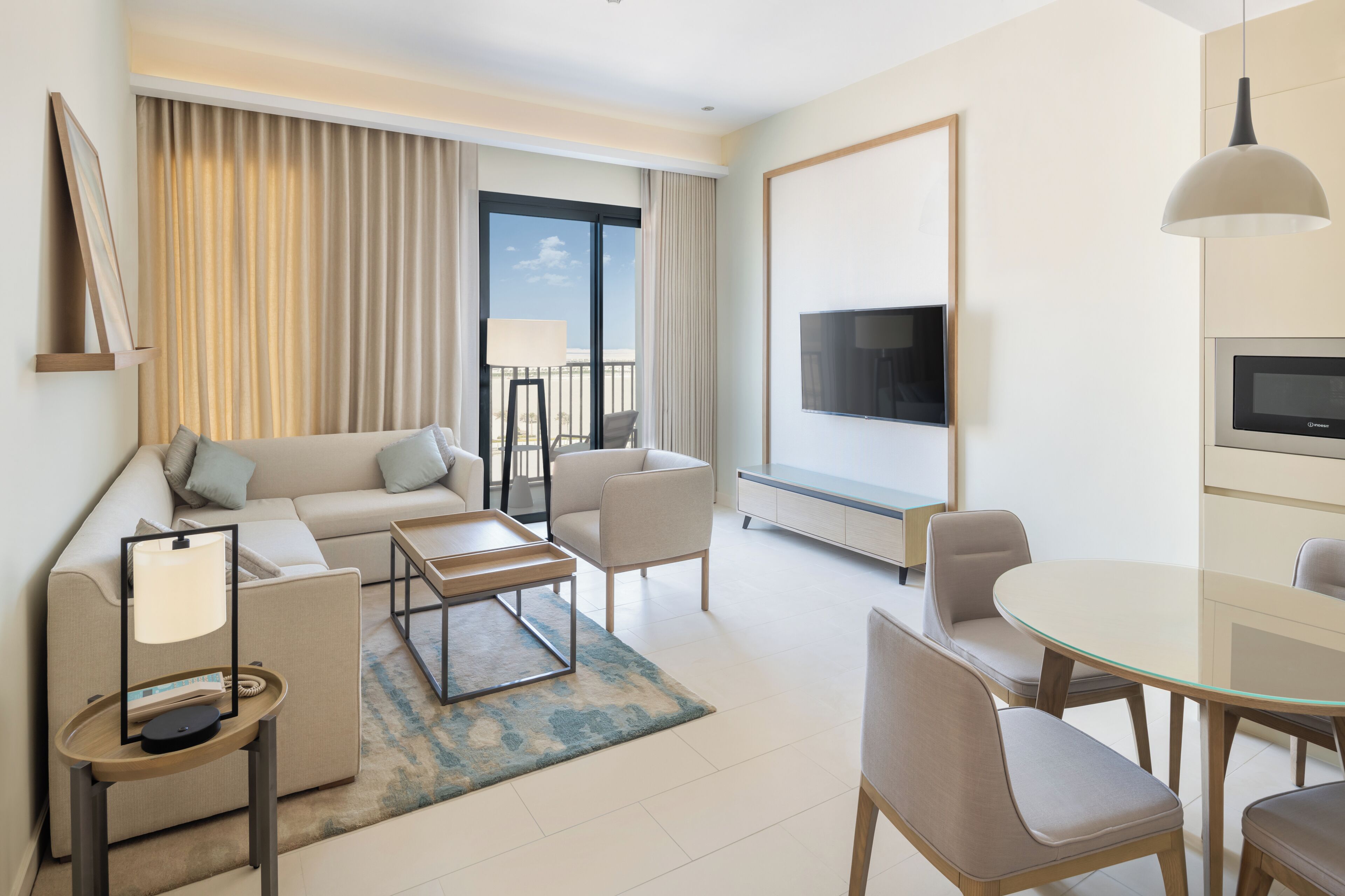 Ein modernes Hotelzimmer mit einer Couch, einem Couchtisch, einem Esstisch mit Stühlen, einem Fernseher und einem Balkon mit Vorhängen.