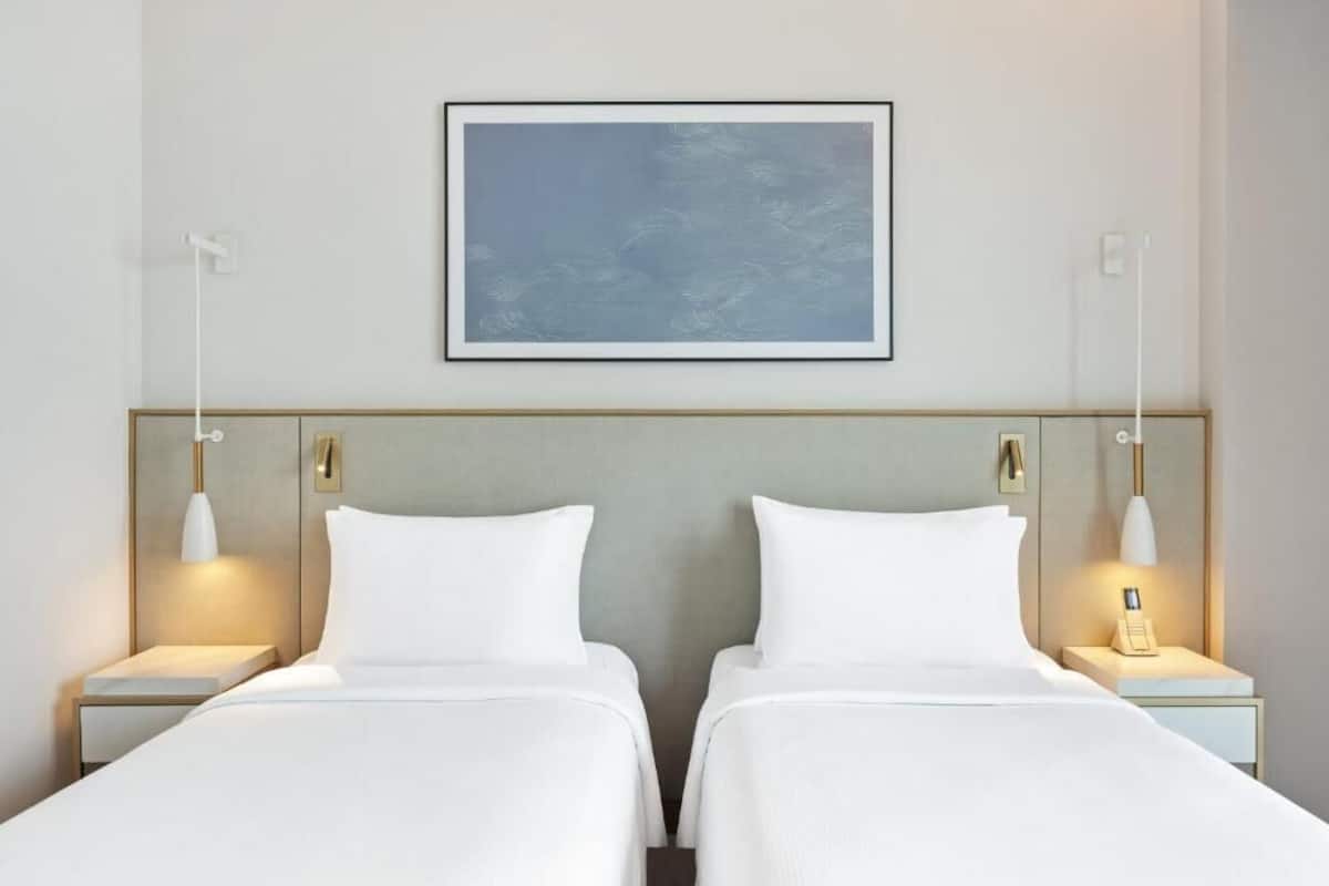 Ein Hotelzimmer mit zwei Betten, einem gerahmten Kunstwerk darüber und Nachttischlampen.