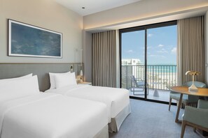 A hotel room with two beds, a balcony with a view of the beach, a dining area, and a painting on the wall. - Vida Beach Resort Marassi Al Bahrain (Manama)