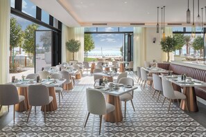 A modern restaurant with a view of the sea, featuring a mix of dining tables and booths, a patterned floor, and large windows. - Vida Beach Resort Marassi Al Bahrain (Manama)