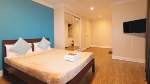 Habitación de hotel con cama, televisor de pantalla plana y baño a la vista a través de una puerta abierta.