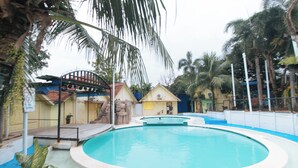Una piscina de forma circular, rodeada por una cerca, palmeras y un pequeño edificio con techo rojo.