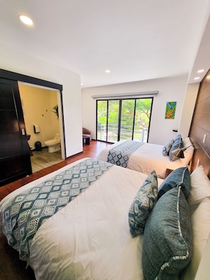 A modern hotel room with two beds, a large window with a view of greenery, a painting on the wall, and a ceiling light. - Burbi Lake Lodge (Cabeceras)