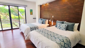 Ein modernes Schlafzimmer mit einem großen Bett, einem Holzkopfende und Blick auf Grün durch große Fenster.