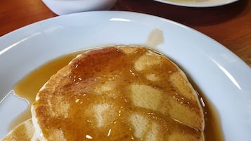 A breakfast plate with pancakes and syrup, a bowl of yogurt with fruit, and a plate of fruit.