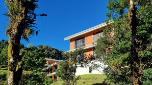 A modern house with a wooden deck leading to a pond, surrounded by lush greenery and trees. - Burbi Lake Lodge (Cabeceras)
