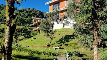 Une maison moderne dotée d’une terrasse en bois donnant sur un étang, le tout entouré d’une végétation luxuriante et d’arbres.