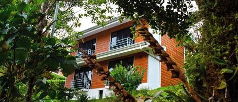 Uma casa moderna de dois andares com uma varanda no segundo andar, rodeada por vegetação exuberante.