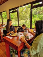 Un comedor con una mesa de madera, sillas y ventanas amplias con vistas a la vegetación.