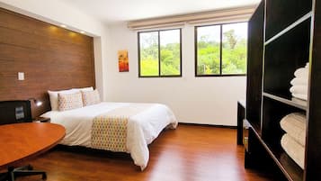 Une chambre d’hôtel équipée d’un lit, d’un bureau, d’une chaise, d’une armoire et de grandes fenêtres donnant sur un paysage verdoyant.