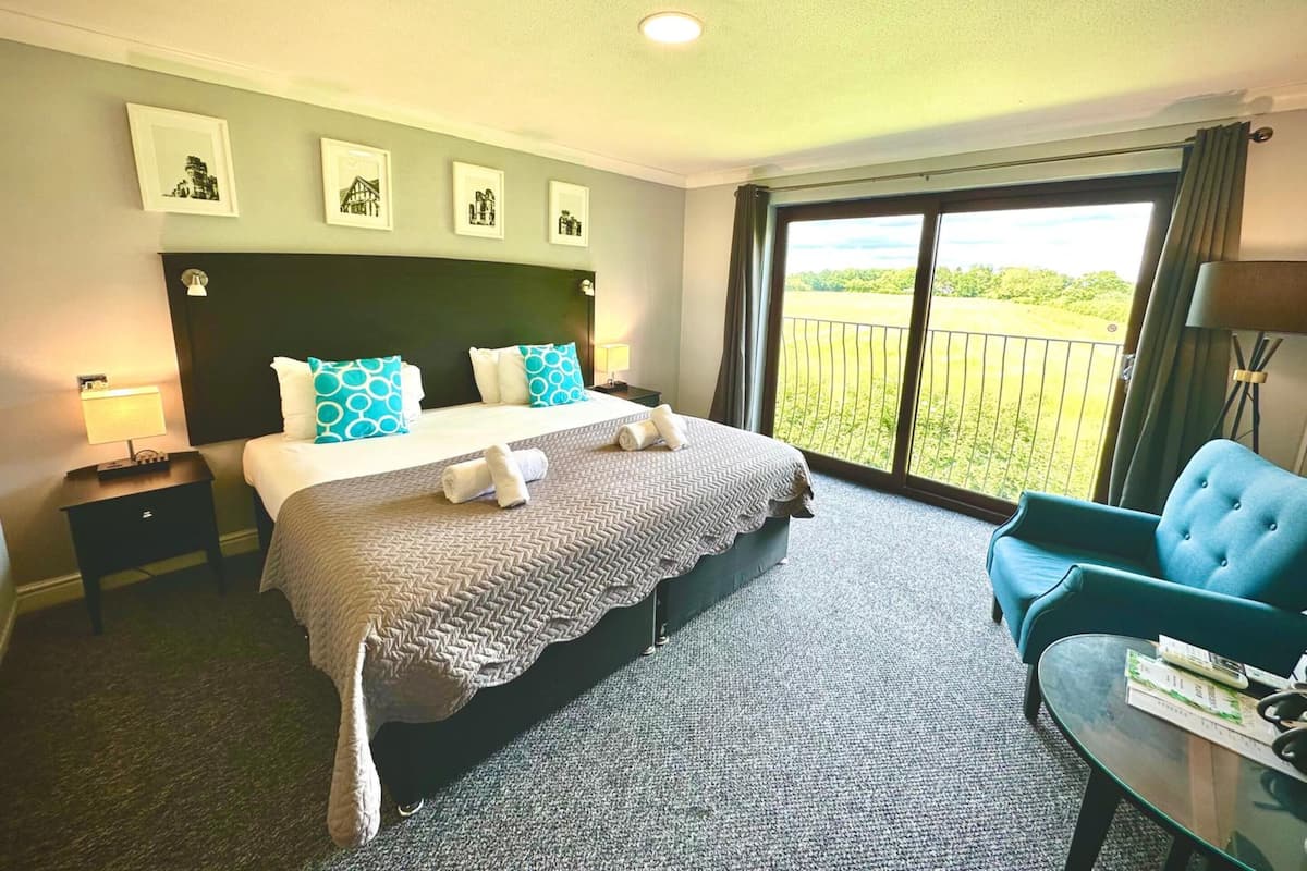A hotel room with a large bed, a balcony with a view, and a seating area.