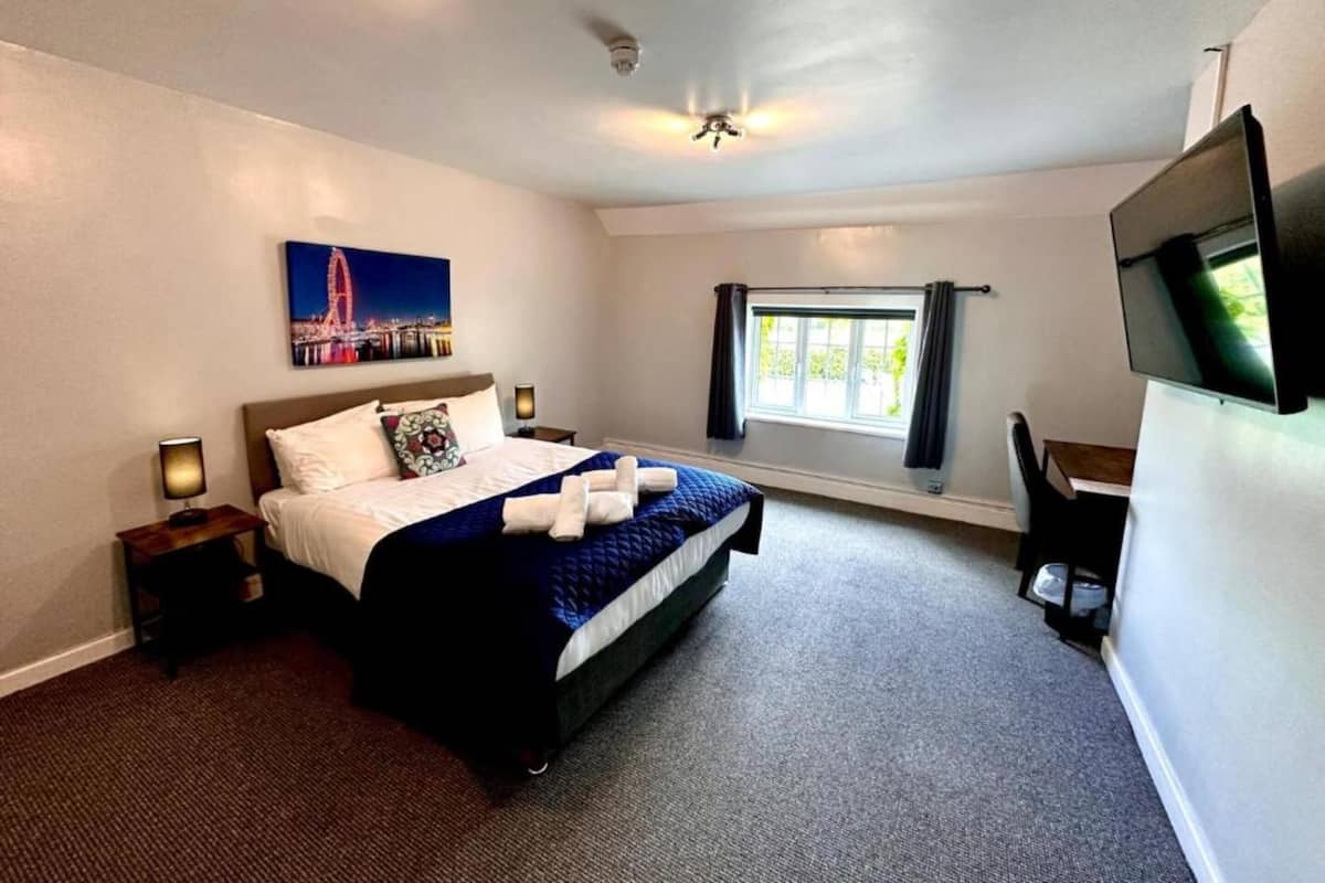 A hotel room with a bed, a TV, a window with curtains, and a painting of a cityscape.