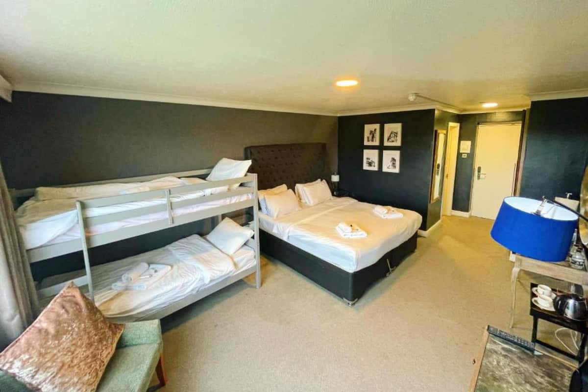 A room with bunk beds, a single bed, a desk with a lamp, and a bathroom door.