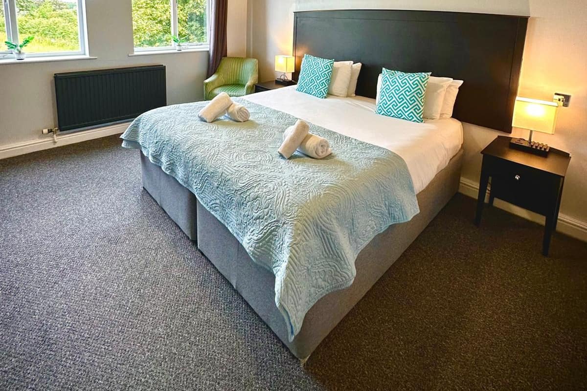 A neatly arranged bedroom with a large bed, two bedside tables, a radiator, and a window with curtains.