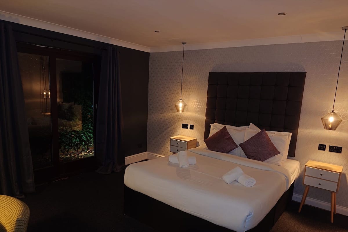 A modern hotel room with a large bed, a nightstand, and a window with curtains.