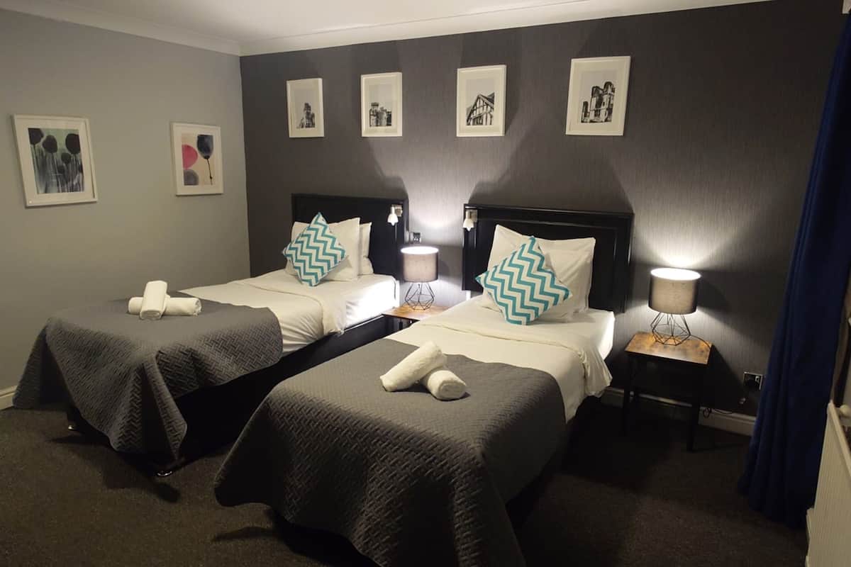 A hotel room with two beds, each with a headboard, bedside tables, and lamps. There are framed pictures on the wall.