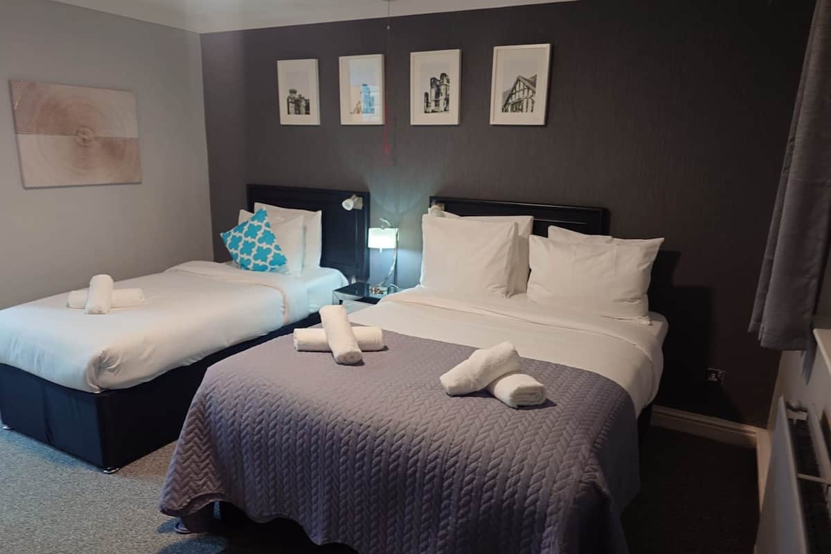 A hotel room with two beds, each with white linens and rolled towels. There are four framed pictures on the wall above the beds.