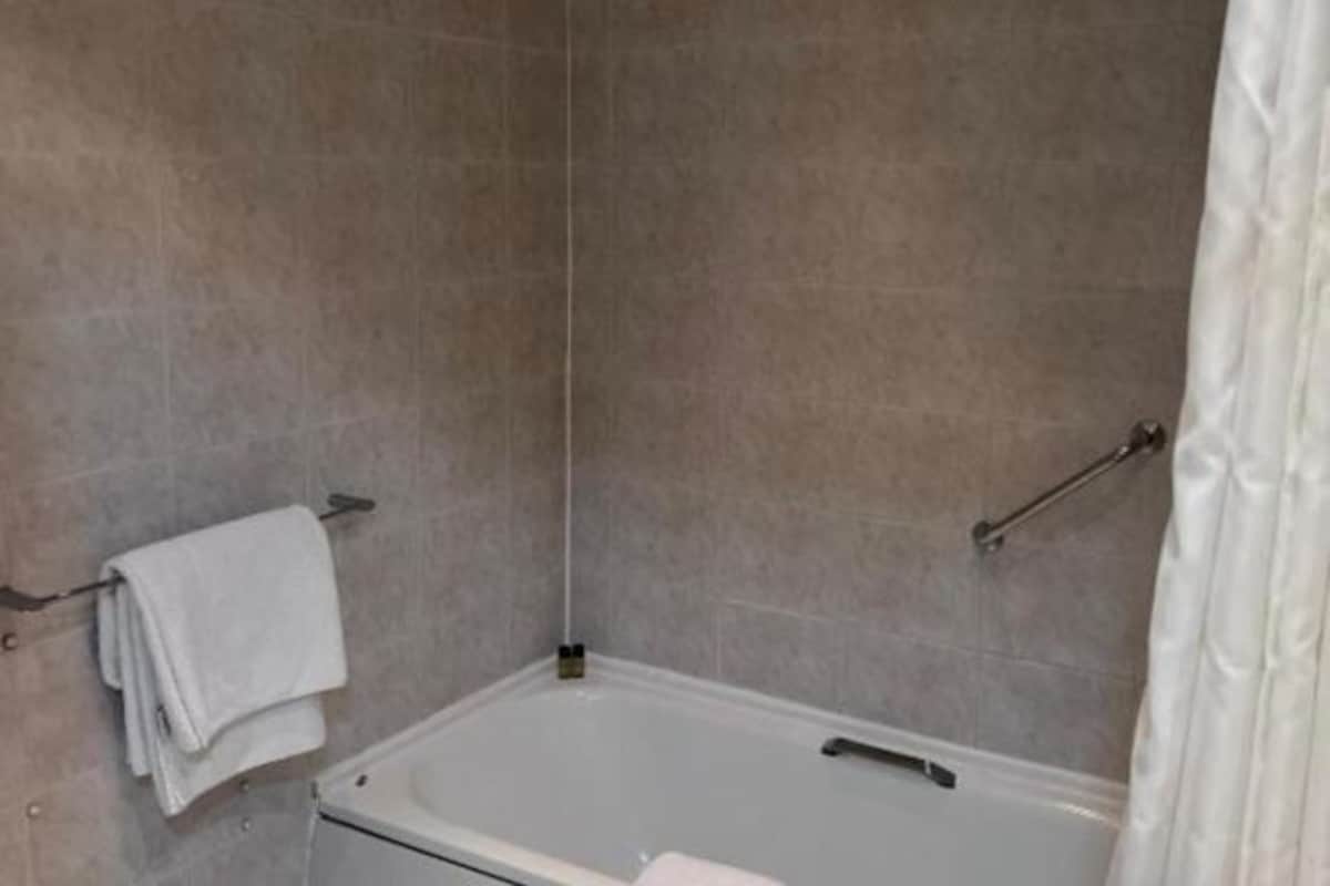 Un baño con bañera, un perchero con una toalla doblada y una cortina de ducha.
