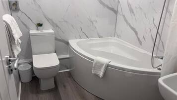 A modern bathroom with a toilet, bidet, and a freestanding bathtub.