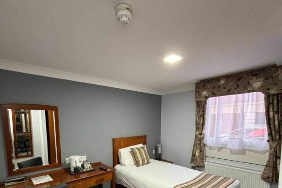 Une chambre à coucher avec un lit, un bureau, une chaise, un miroir et une fenêtre avec des rideaux.