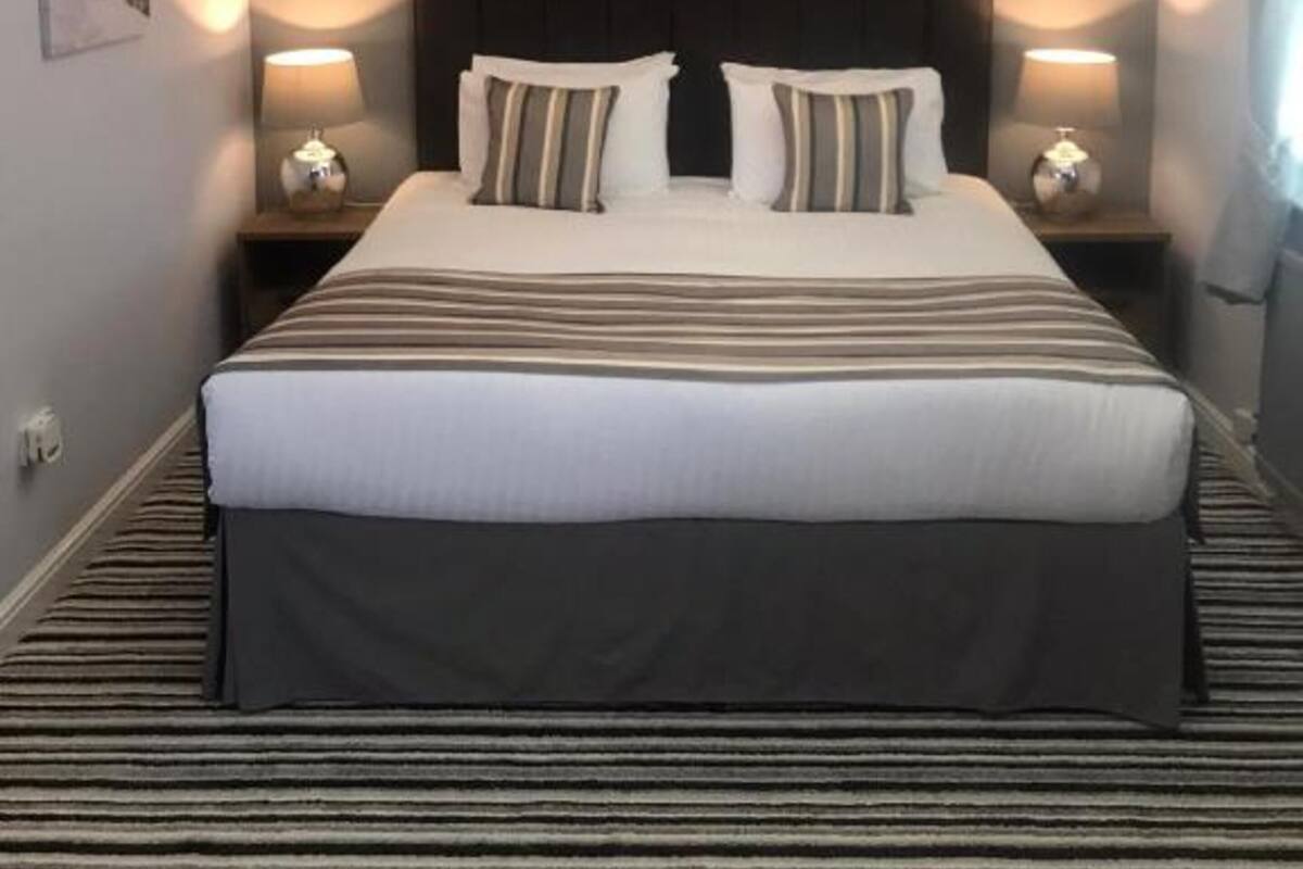 Une chambre d’hôtel avec un grand lit, deux tables de chevet et une tête de lit.