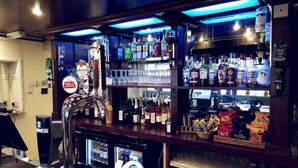 Eine Bar mit mehreren Regalen voller Spirituosenflaschen, einem Zapfhahn für Bier und einem Kühlschrank.