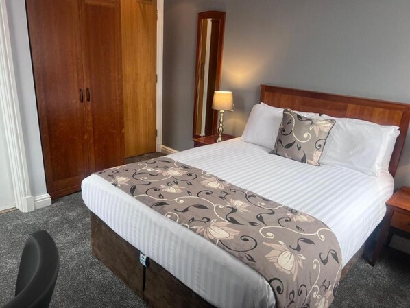 A hotel room with a large bed, a wooden wardrobe, a nightstand with a lamp, and a carpeted floor. - Dancenter East Midlands Airport (Derby)