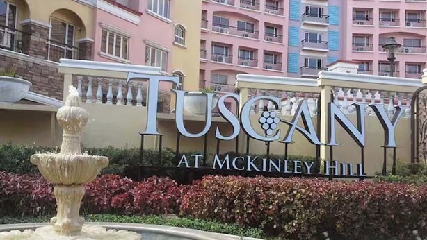 Une enseigne indiquant « Toscane à McKinley Hill », avec une fontaine au premier plan.