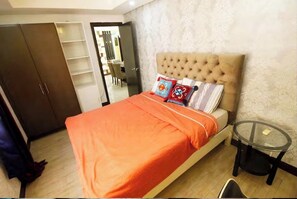 Une chambre à coucher comprenant un lit, une armoire, une table en verre et une porte donnant sur une salle de bain.