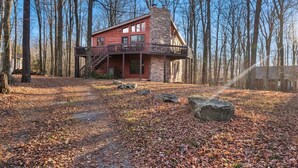 A cabin with a stone chimney, a balcony, and a forested backdrop. - The Alpine Arena (Clifton Township)