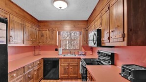 A kitchen with wooden cabinets, a black microwave, a stove, and a toaster. - The Alpine Arena (Clifton Township)