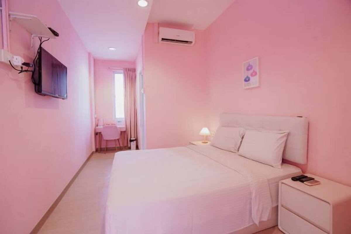 A pink-themed hotel room with a bed, bedside table, and a TV mounted on the wall.