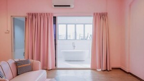 Una stanza con pareti rosa, un divano bianco, un tavolino da caffè rotondo in marmo e vista su una vasca da bagno bianca tramite una porta in vetro.