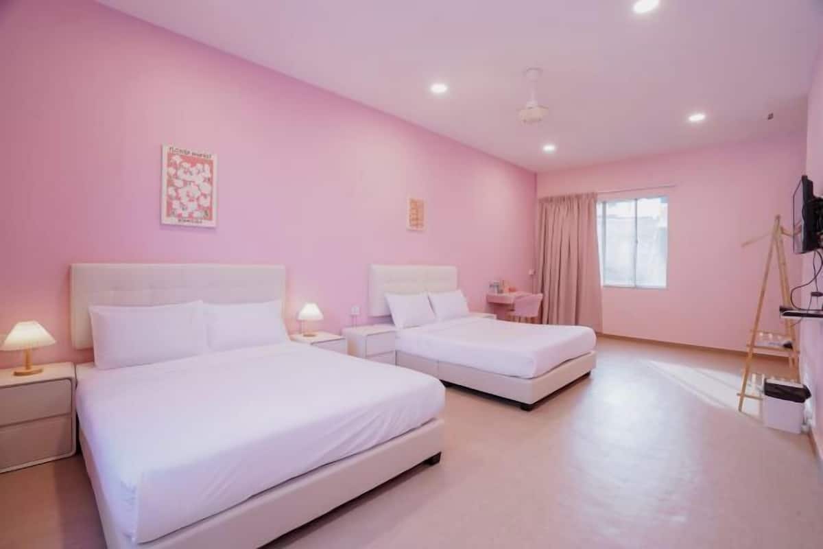 A pink-themed hotel room with two beds, a desk, and a window.