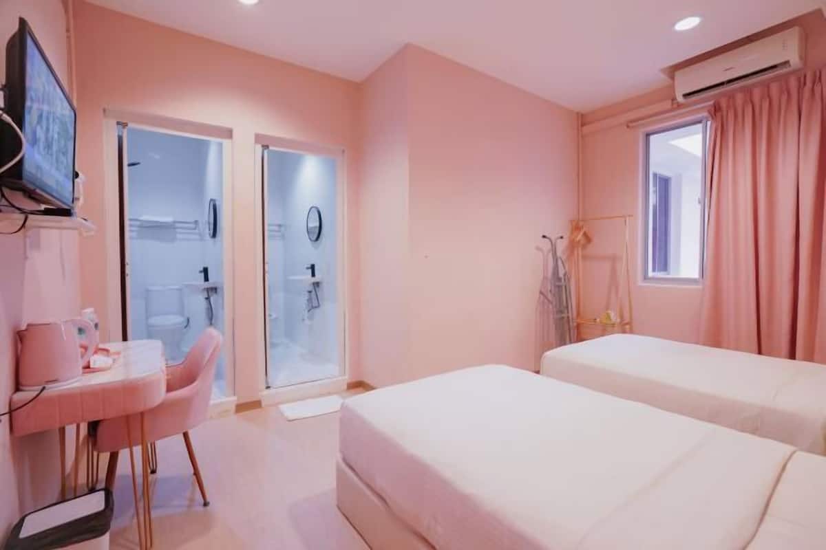 A hotel room with two beds, a desk with a chair, a television, and a bathroom visible through an open door.
