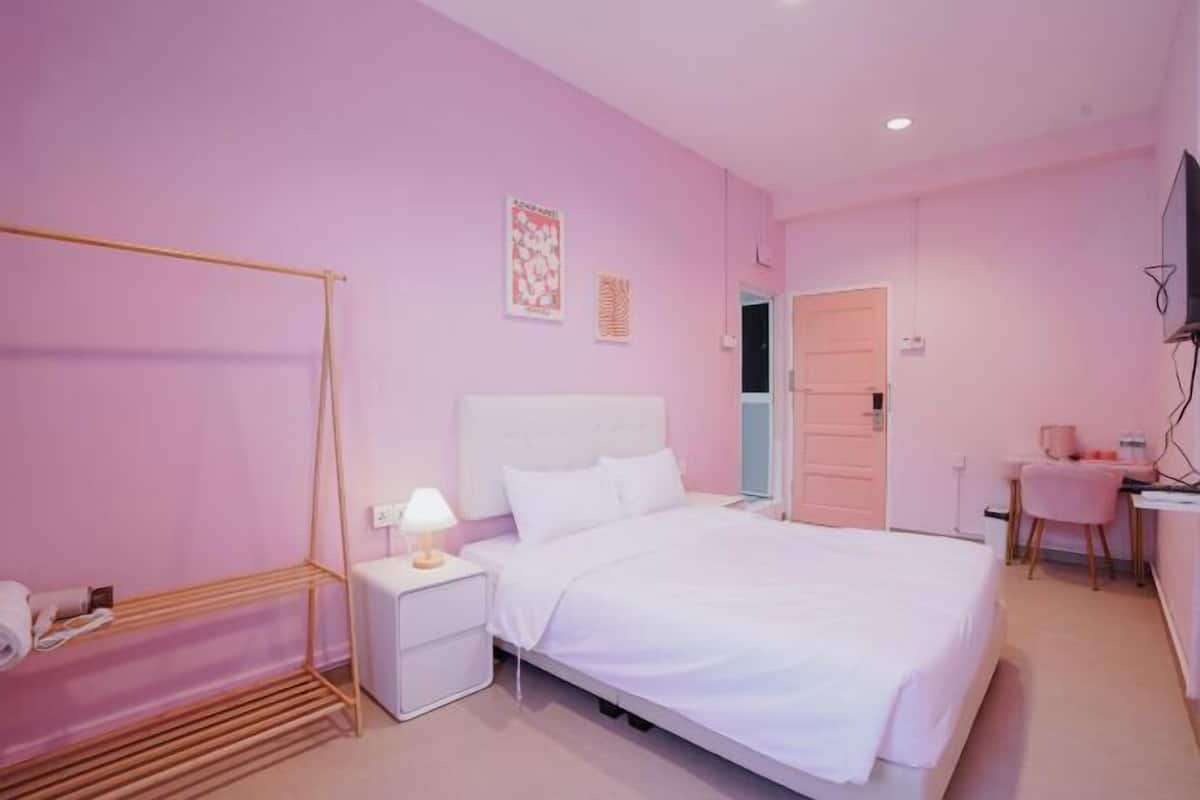 A pink-themed bedroom with a bed, bedside table, and a desk with a chair.