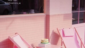Facciata di un edificio con piastrelle rosa, una finestra, una sedia rosa e una torta su un tavolino.