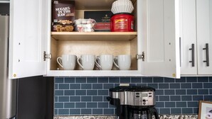 Una cocina con cafetera, repisa con azúcar, bolsitas de té y una caja de Folgers.