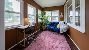 Una habitación con un escritorio, una silla azul, una planta grande y un tapete rosa.