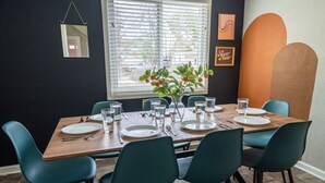 Un comedor con mesa de madera dispuesta para seis personas, sillas color turquesa y un jarrón con flores anaranjadas.