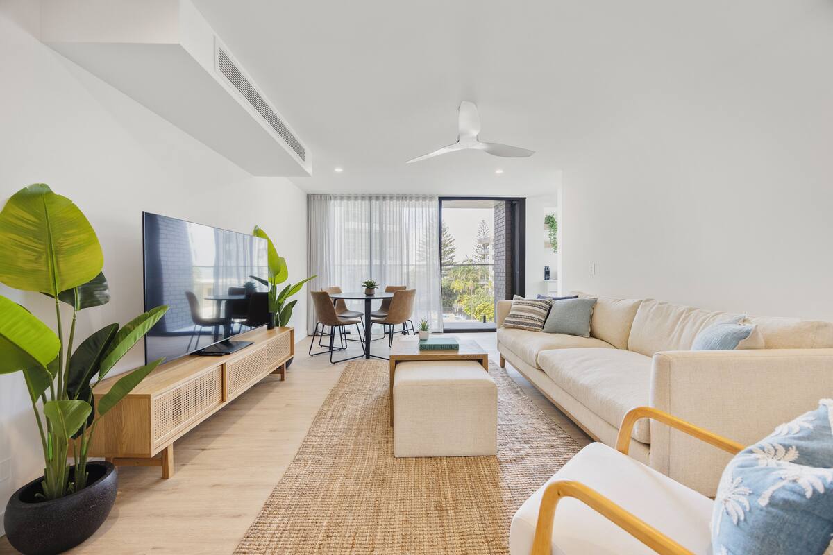 Una sala de estar moderna con sofá, mesa de centro, televisor y zona de comedor.